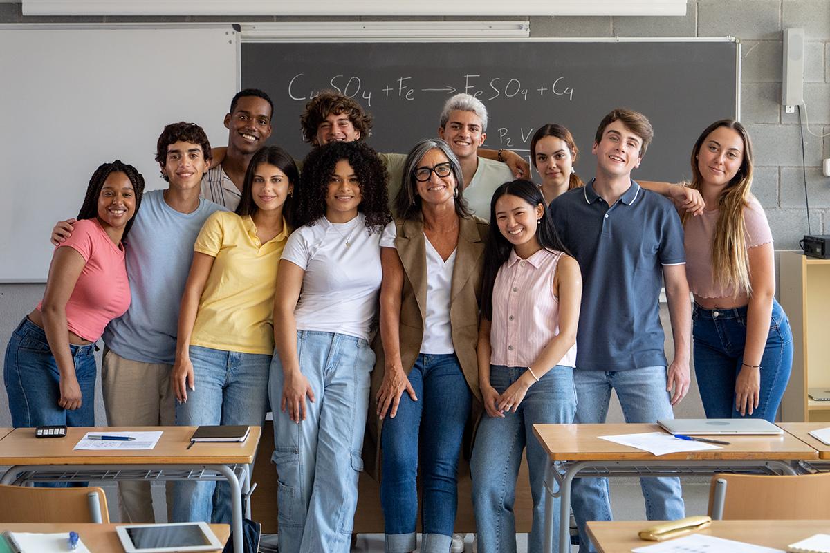 Portrait of a group of diverse teenage students and a female teacher smiling looking at camera in a class. High school, school year, university